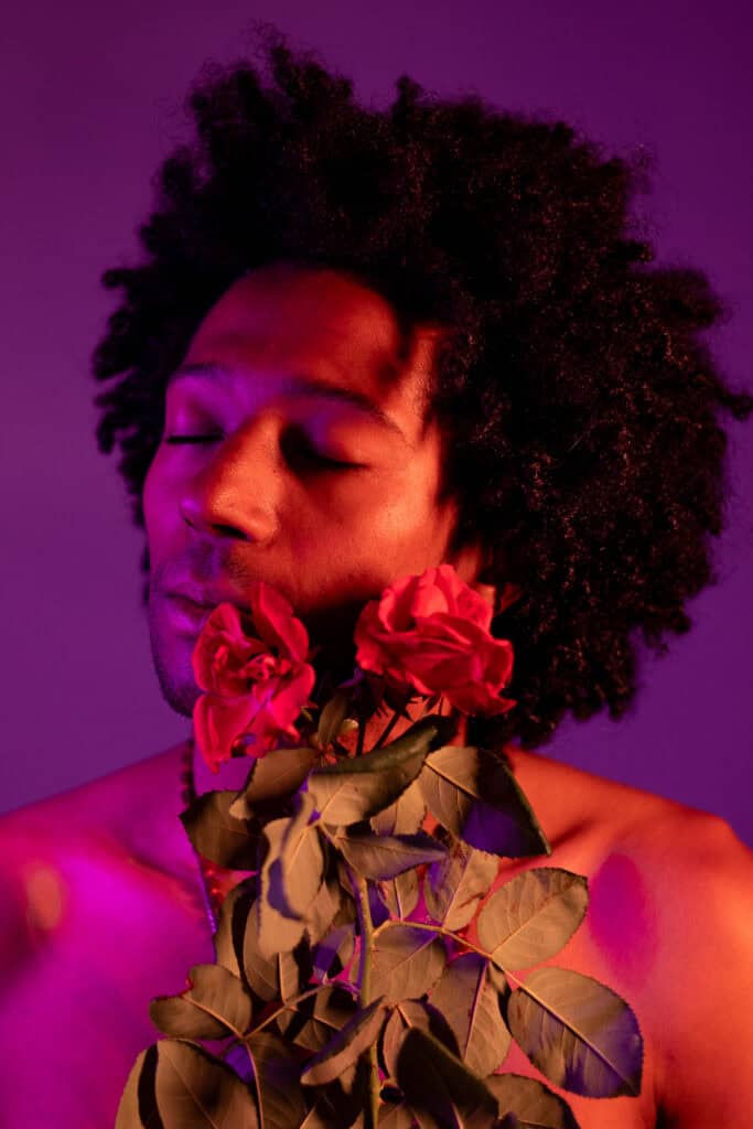 Mulher com cabelo afro segurando rosas, iluminação roxa, expressão serena.
