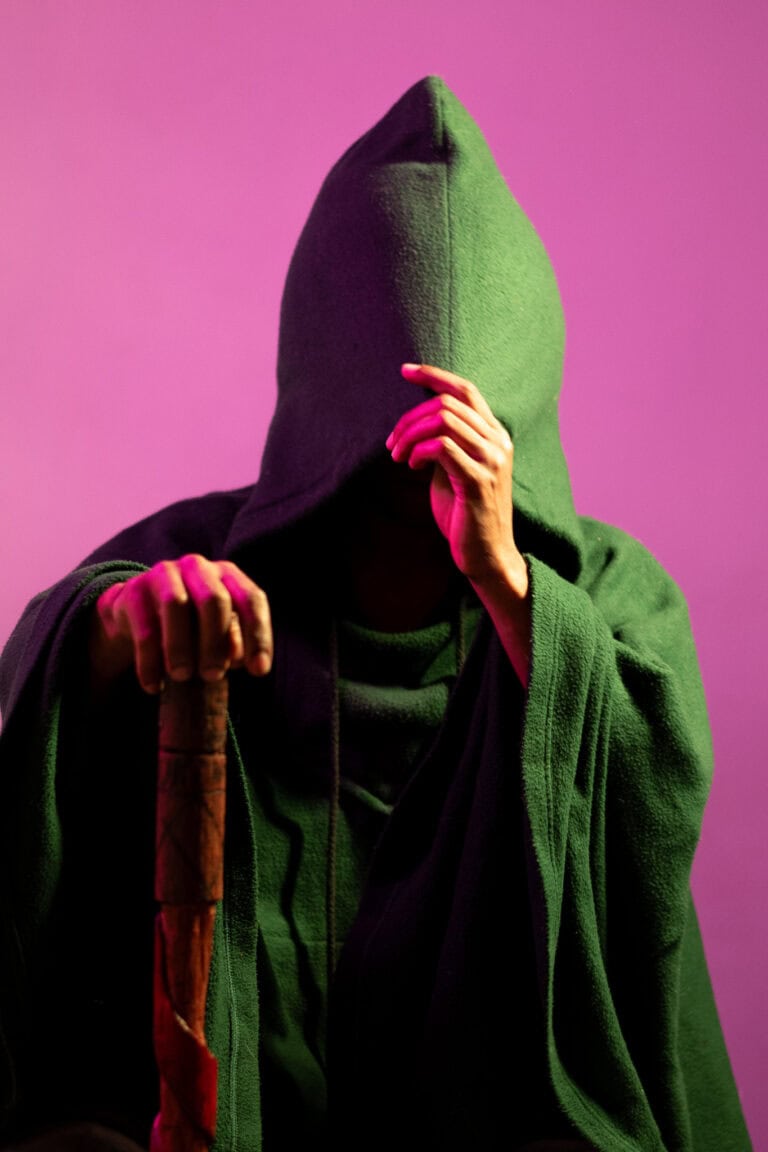 Assassino misterioso com capuz verde e bastão, fundo roxo.