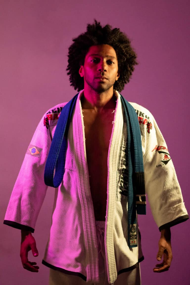 Foto de um praticante de Jiu-Jitsu com faixa azul, vestindo kimono branco, em fundo colorido vibrant.