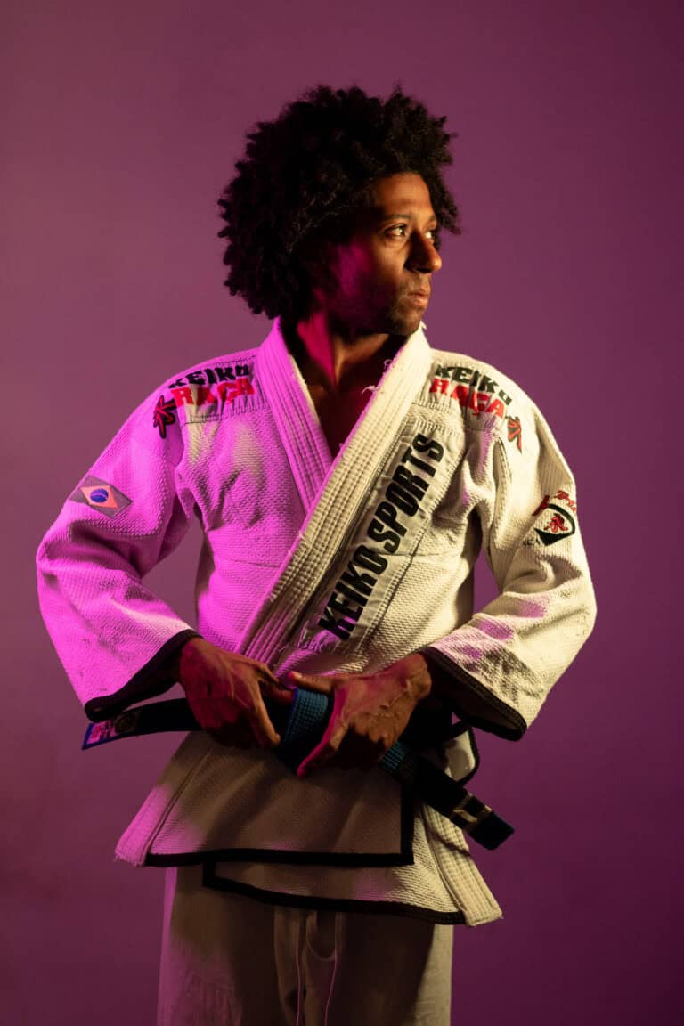 Treinador de Jiu-Jitsu com kimono branco e faixa preta, posando com foco e determinação.