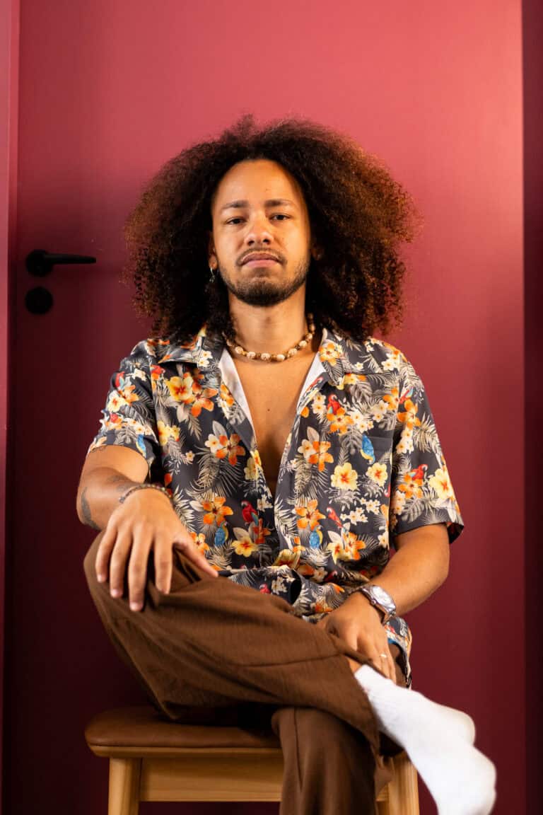 Retrato de homem com cabelo afro, estilo casual, usando camisa floral e acessórios.