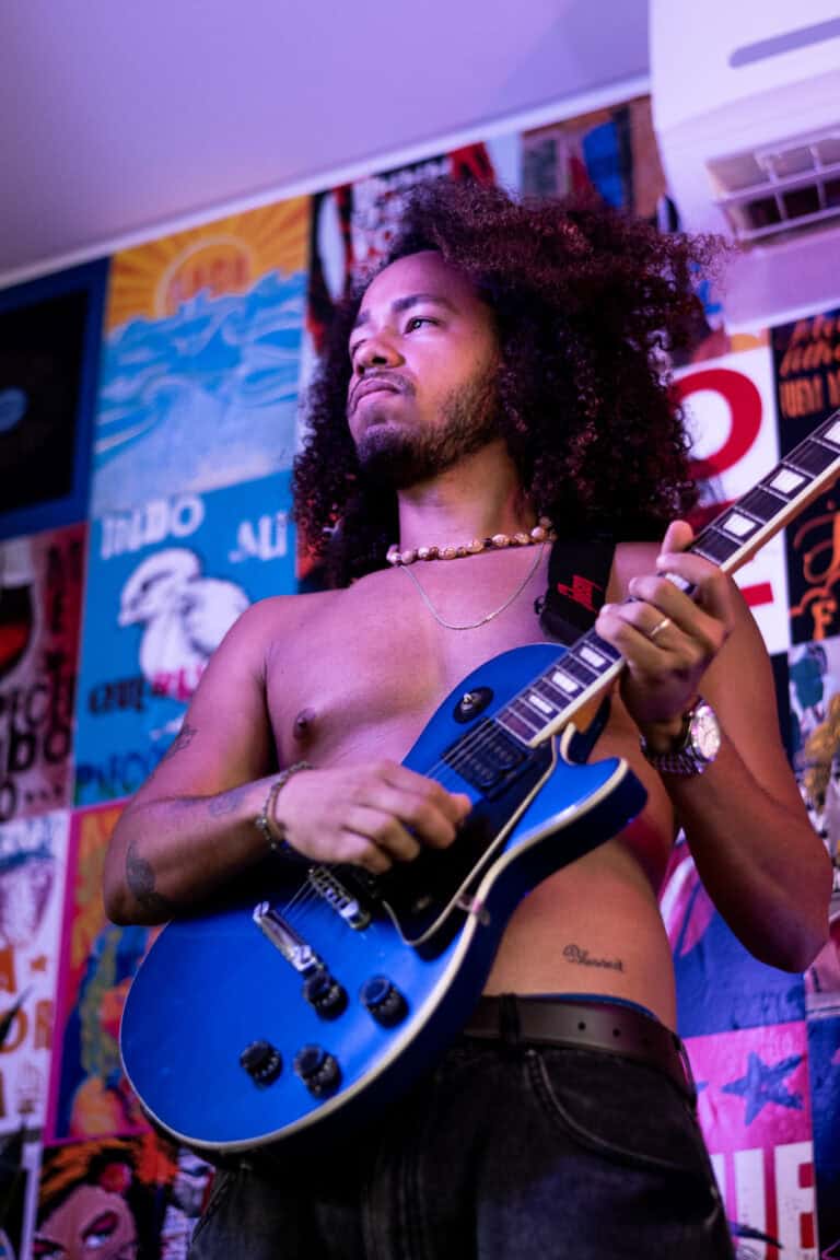 Guitarrista com cabelo afro tocando guitarra elétrica em show ao vivo.