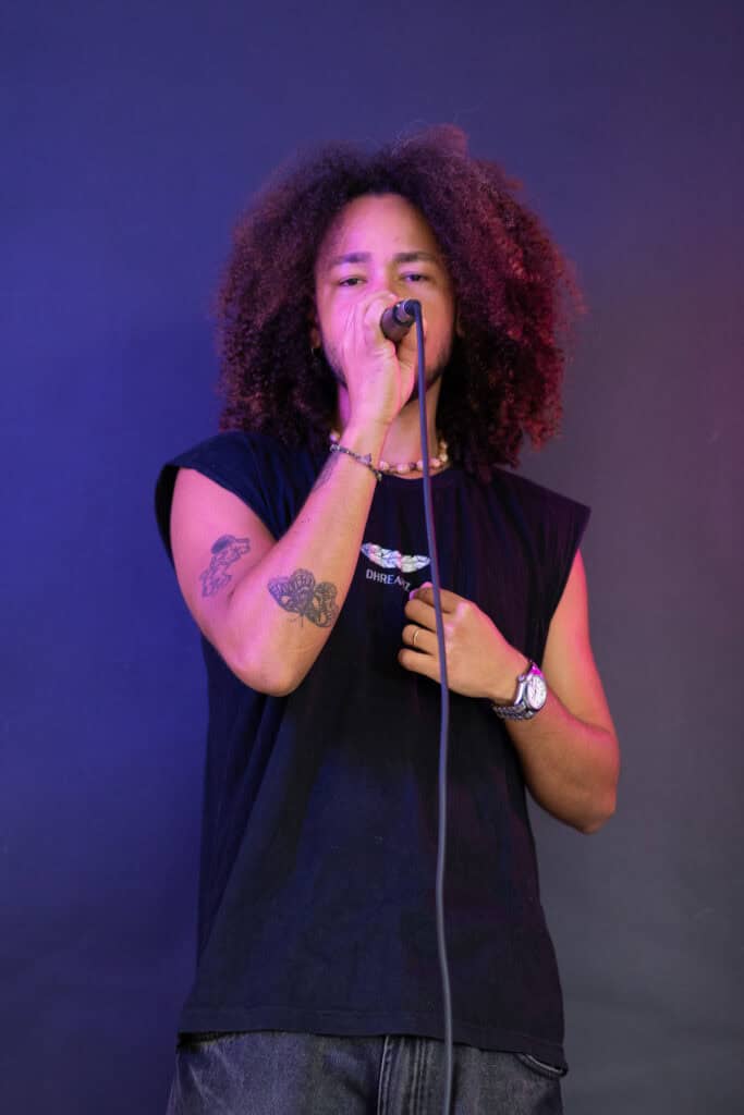 Cantora com cabelo afro segurando microfone em apresentação ao vivo.