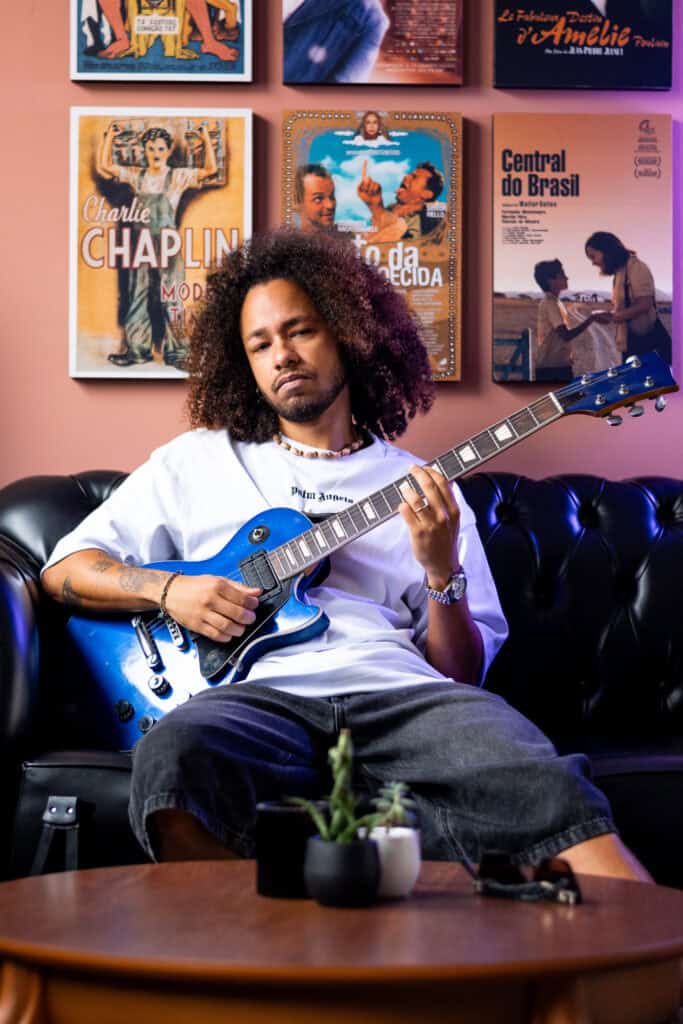 Imagem de um jovem músico com guitarra azul em ambiente artístico.
