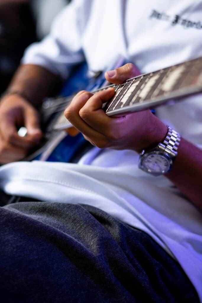 Guitarrista tocando guitarra em show ao vivo, foco na mão e instrumento musical.