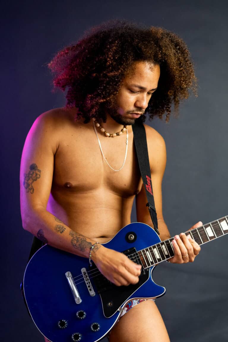 Guitarrista com cabelo afro tocando guitarra azul em estúdio com iluminação suave.