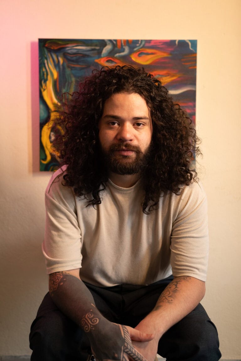 Guilherme Marques, fotógrafo profissional, posando em estúdio com obra de arte ao fundo.