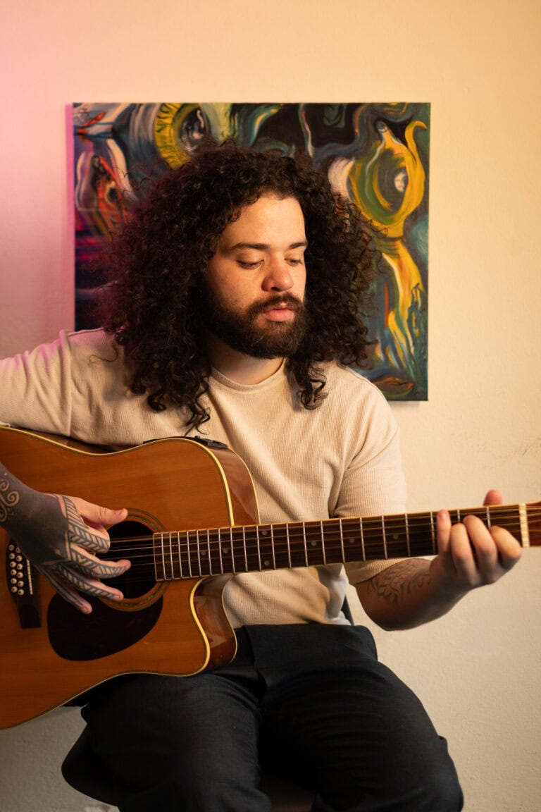 Fotógrafo Guilherme Marques tocando violão em ambiente artístico.