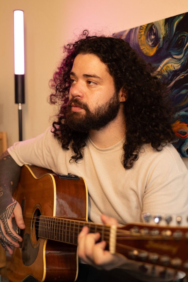 Imagem de um músico com cabelo cacheado tocando violão.