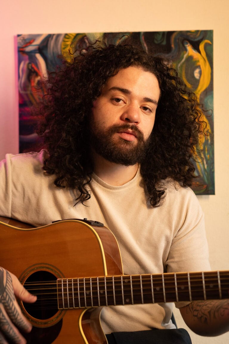 Fotógrafo Guilherme Marques tocando violão em ambiente artístico.