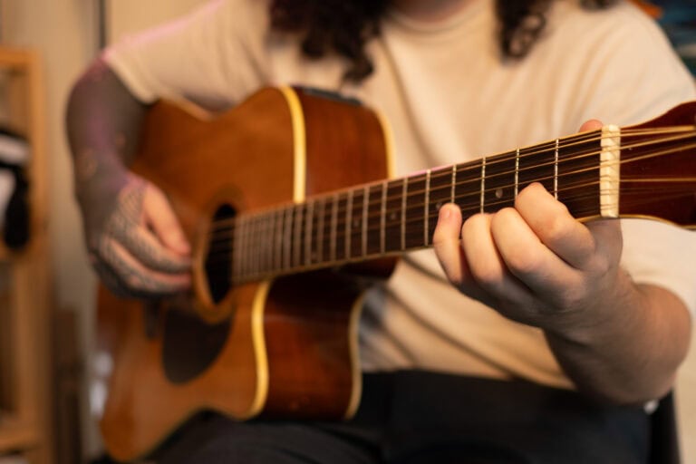 Guitarrista tocando violão em ambiente interno, foco na mão e instrumento.
