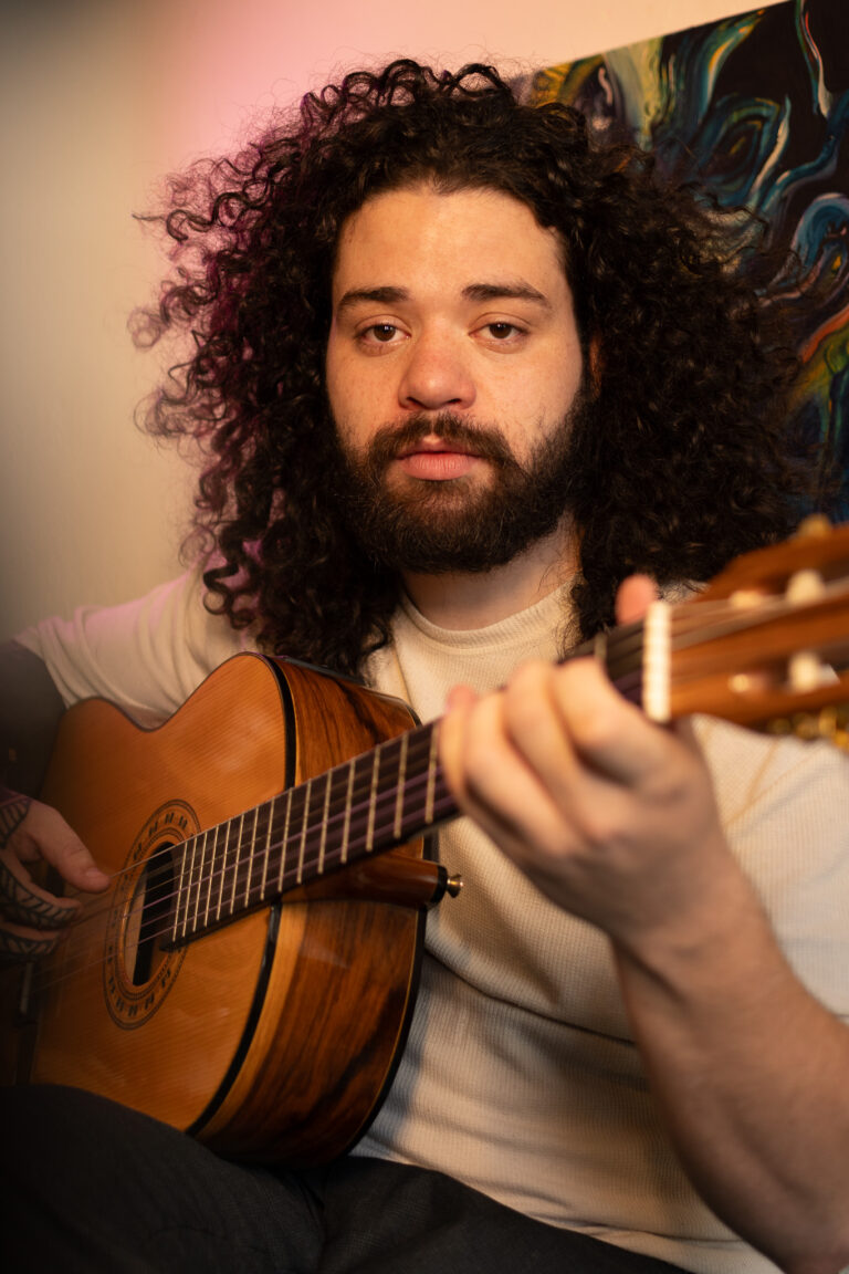 Fotógrafo Guilherme Marques tocando violão em ambiente artístico.
