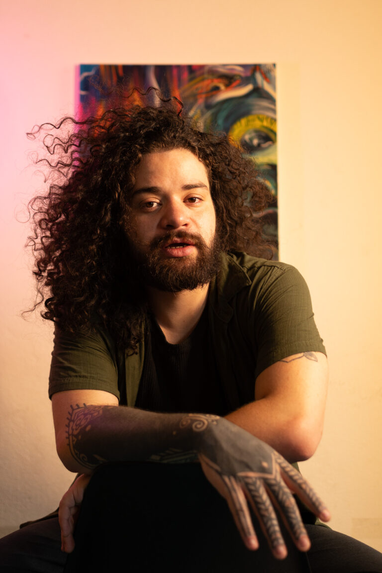 Fotógrafo Guilherme Marques retrato com cabelo cacheado e tatuagens, em estúdio com arte moderna ao.