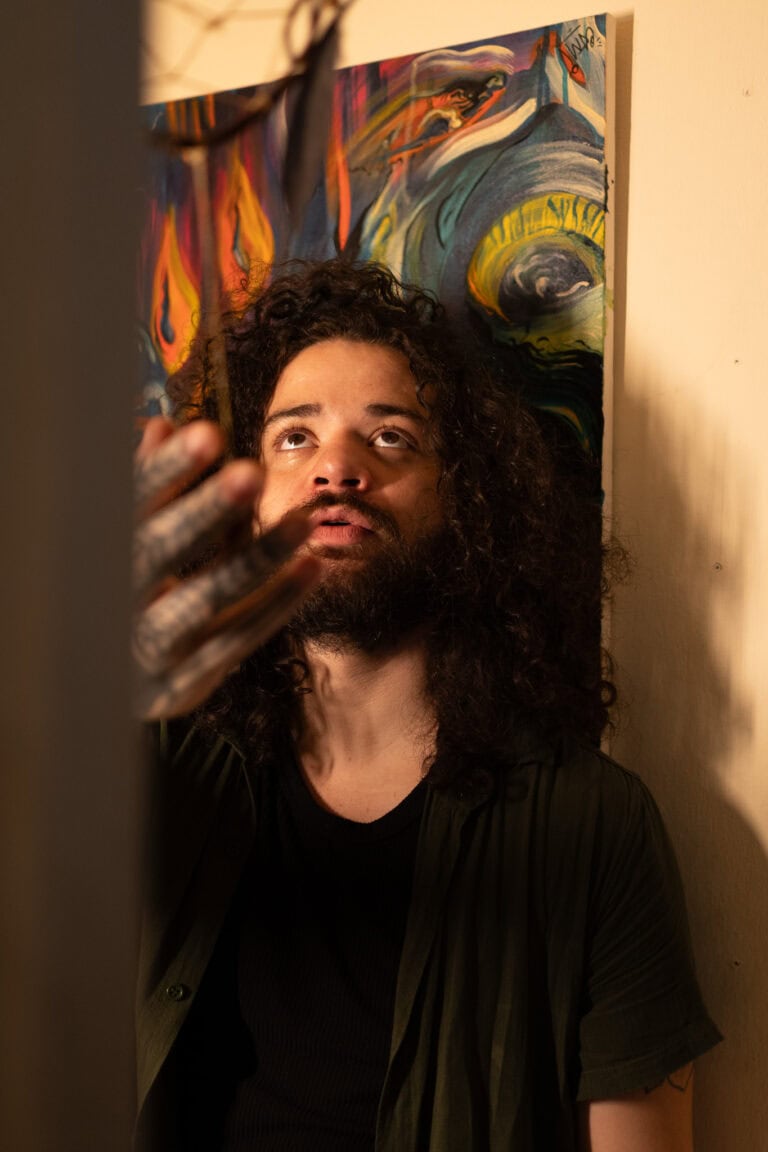 Retrato de artista com fundo artístico, foco na expressão facial e cabelo cacheado.