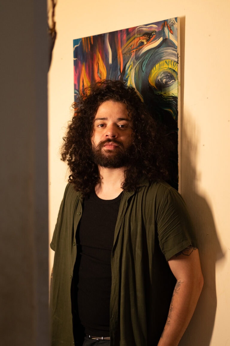 Fotógrafo Guilherme Marques em ensaio artístico com pintura colorida ao fundo.