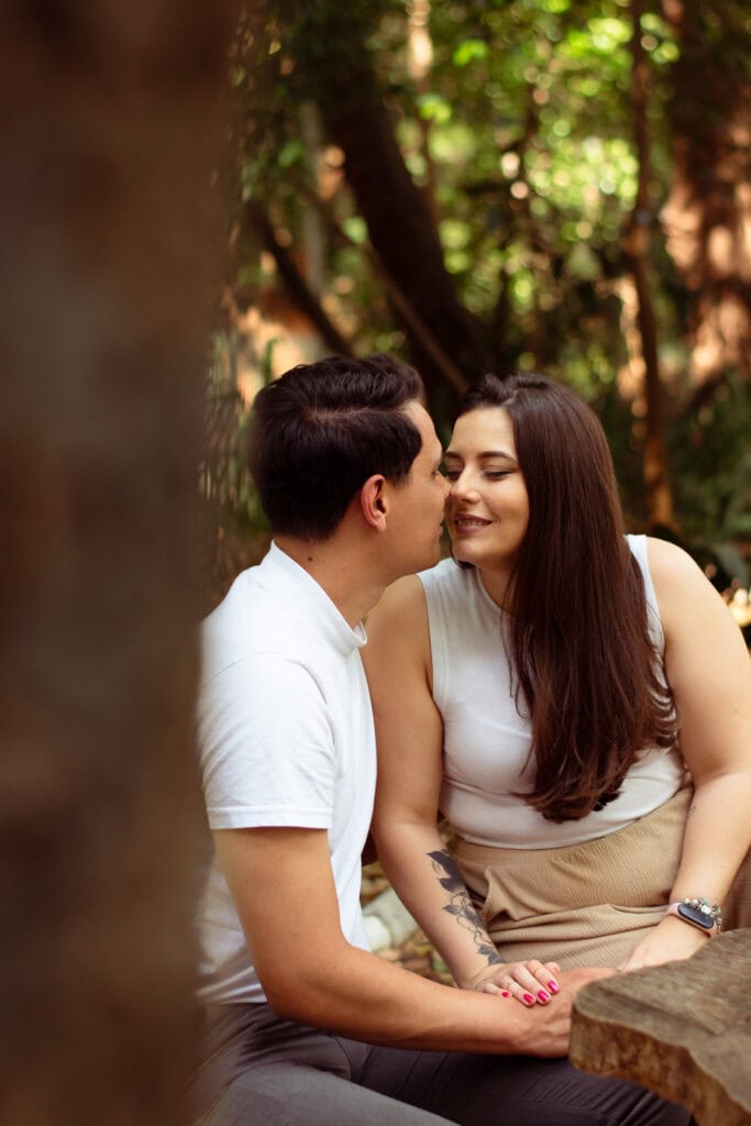 Imagem de casal sorridente em ensaio ao ar livre em parque de São Paulo, com árvores e natureza ao f.