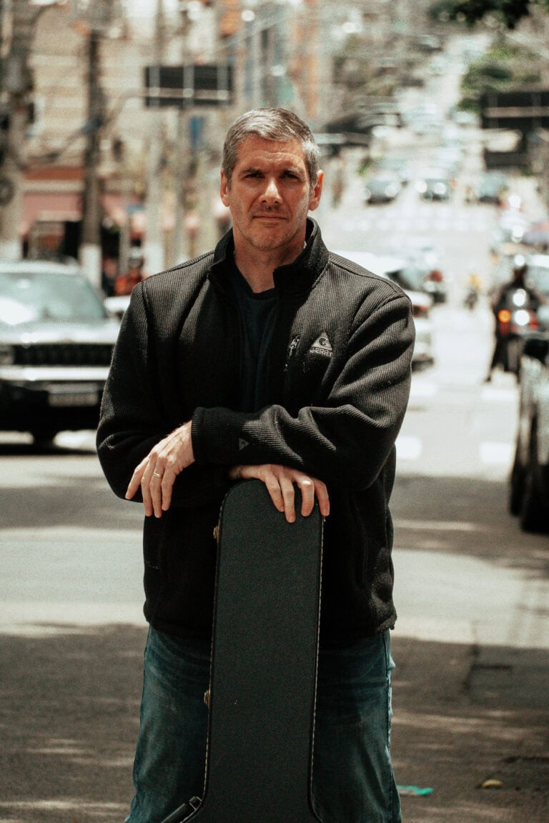 Fotógrafo Guilherme Marques segurando câmera na rua movimentada.