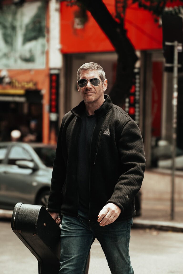 Fotógrafo Guilherme Marques em rua urbana com câmera e mala de equipamento.