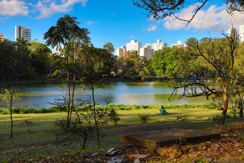 Praia urbana com lago, árvores e pessoas relaxando ao ar livre.