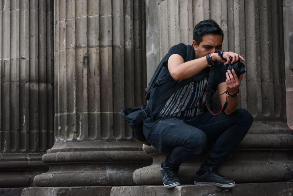 A photographer crouches while capturing images near historic columns in Santiago de Querétaro.