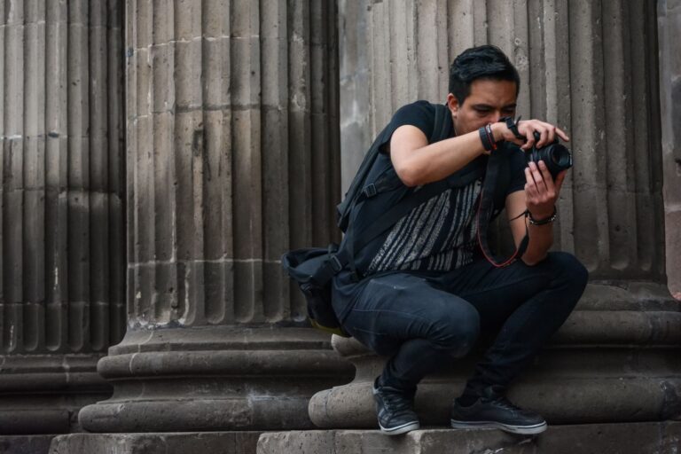 A photographer crouches while capturing images near historic columns in Santiago de Querétaro.