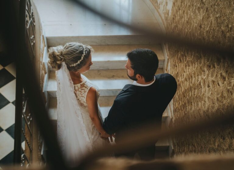 Romantic wedding couple in elegant attire descending a spiral staircase indoors.