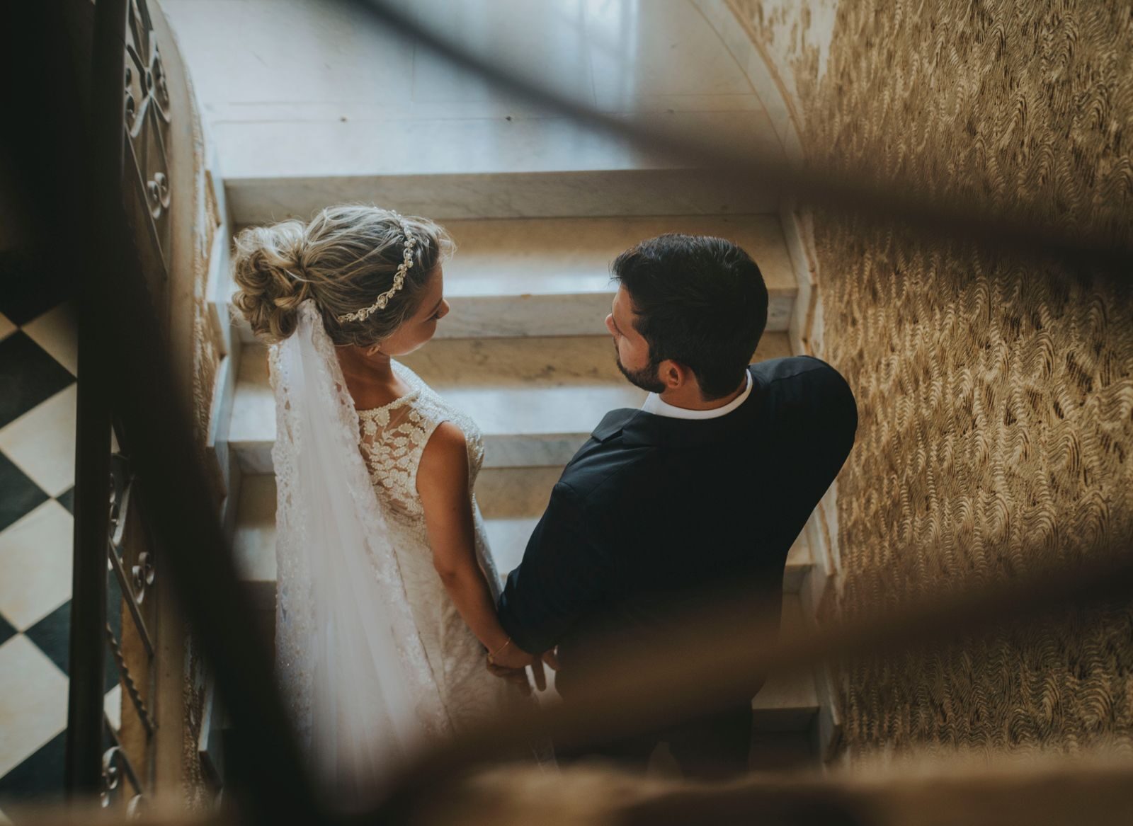Romantic wedding couple in elegant attire descending a spiral staircase indoors.