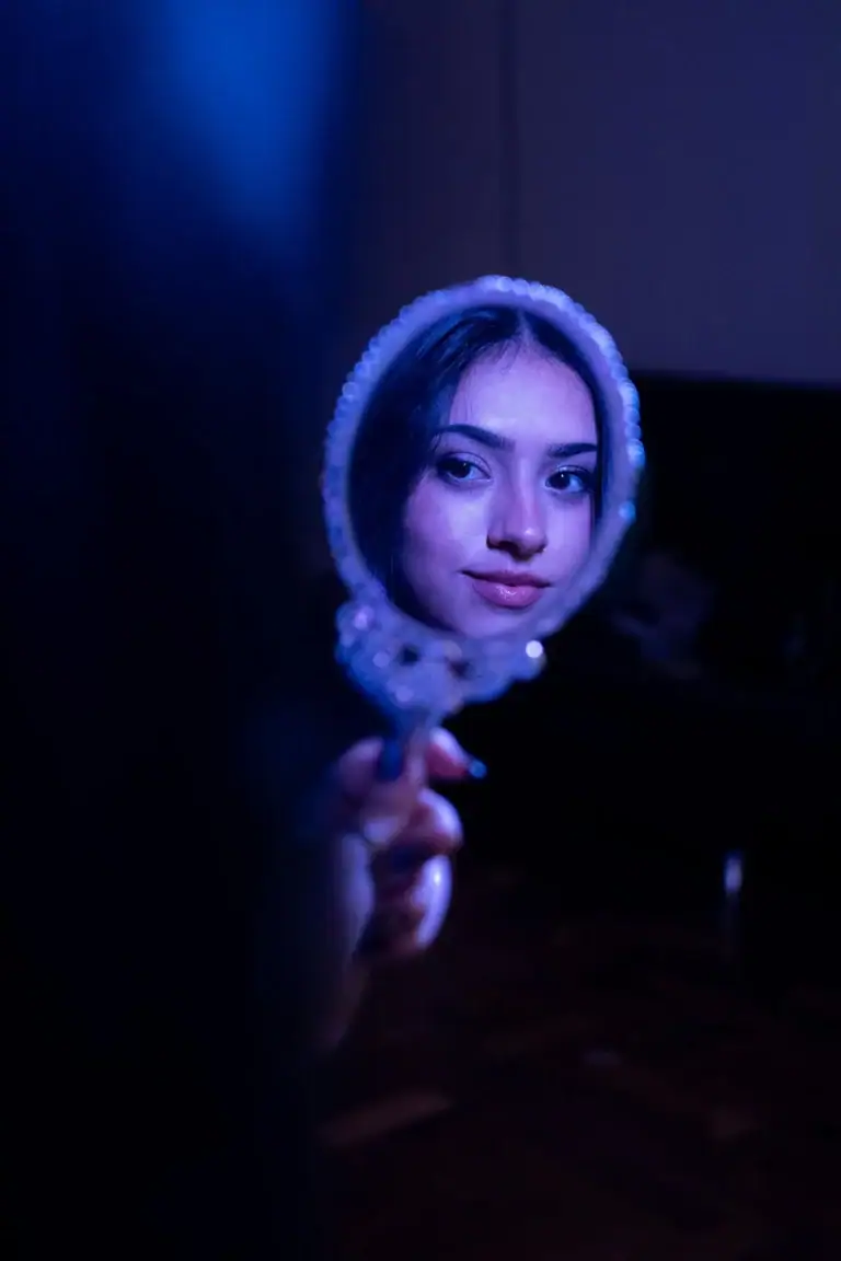 Retrato de uma jovem mulher segurando um espelho, iluminação azul escura.