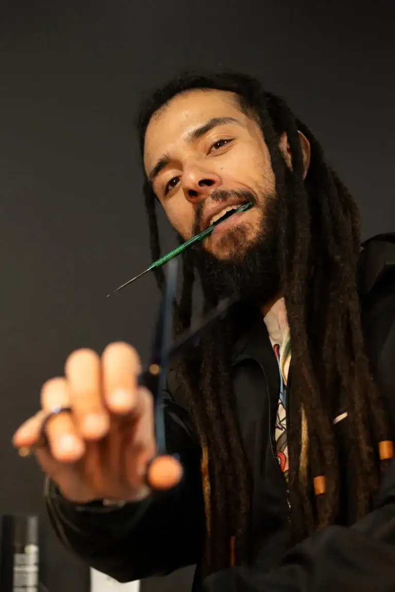 Fotógrafo com dreadlocks segurando uma caneta, sorrindo para a câmera.