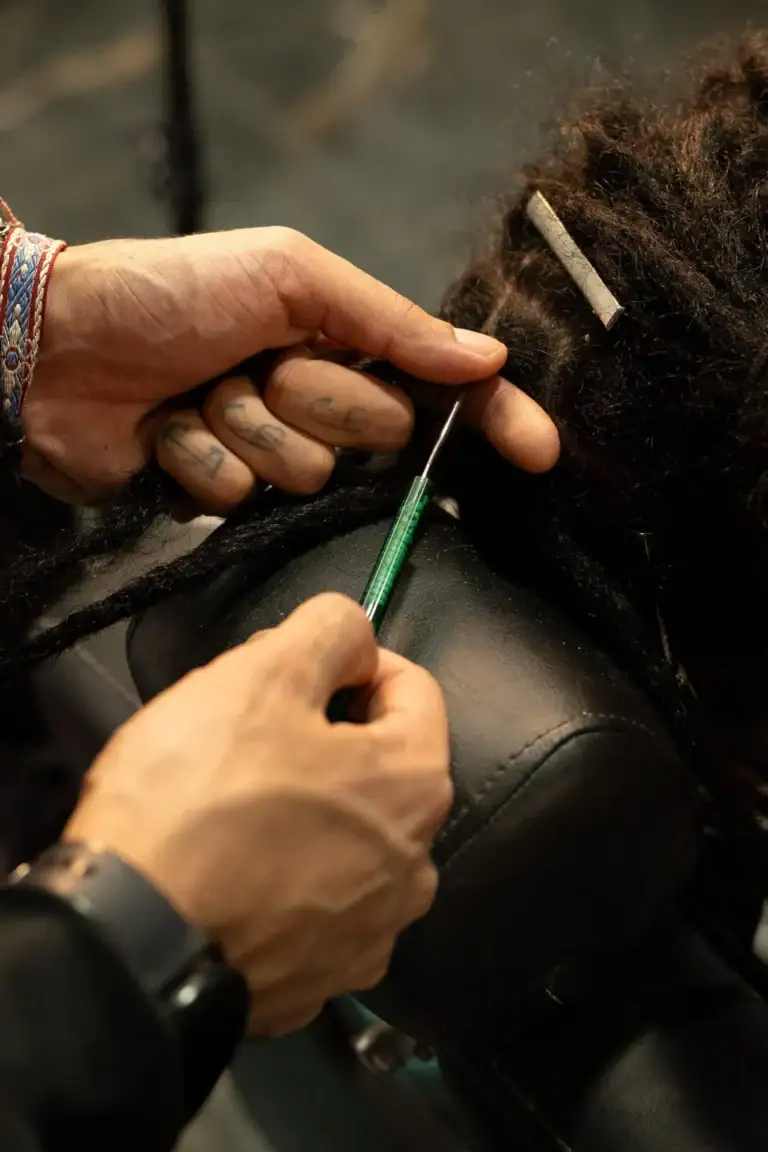 Barbeiro fazendo penteado com agulha em cabelo dreadlock.