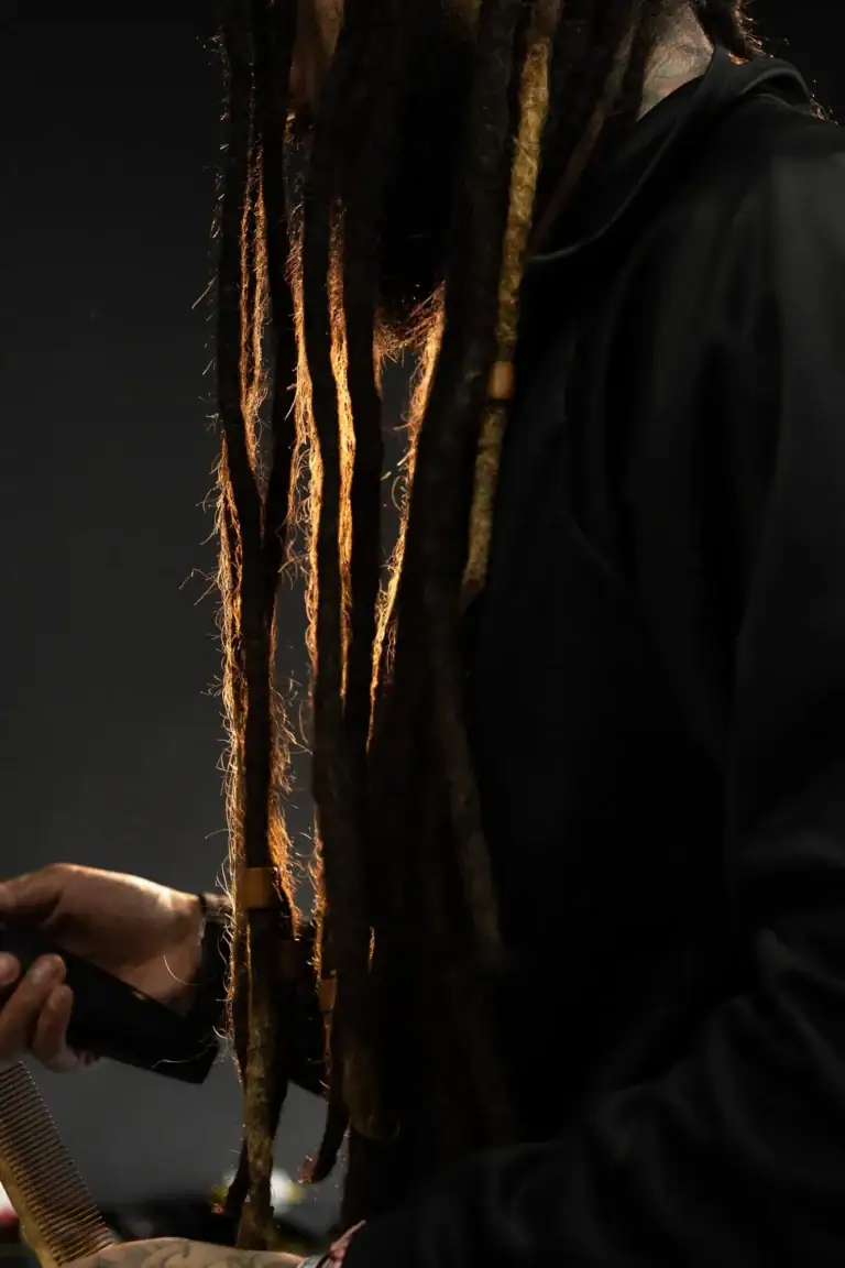 Cabelos dreadlocks longos e coloridos com pessoa de roupa preta ao fundo.