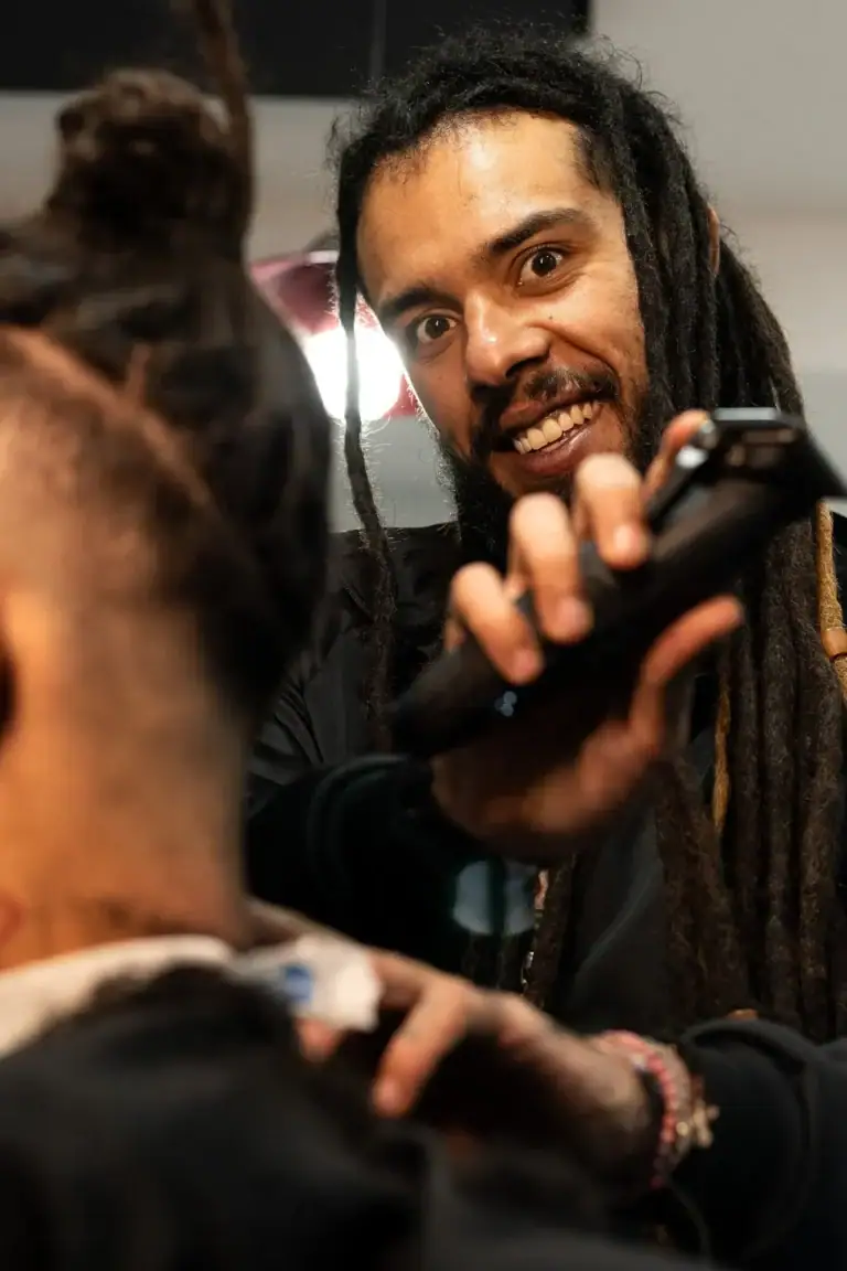 Fotógrafo com dreadlocks sorrindo, segurando uma câmera em ambiente interno.
