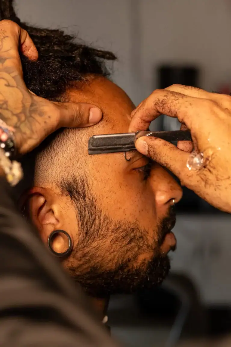 Homem recebendo corte de cabelo com foco na navalha e pente.
