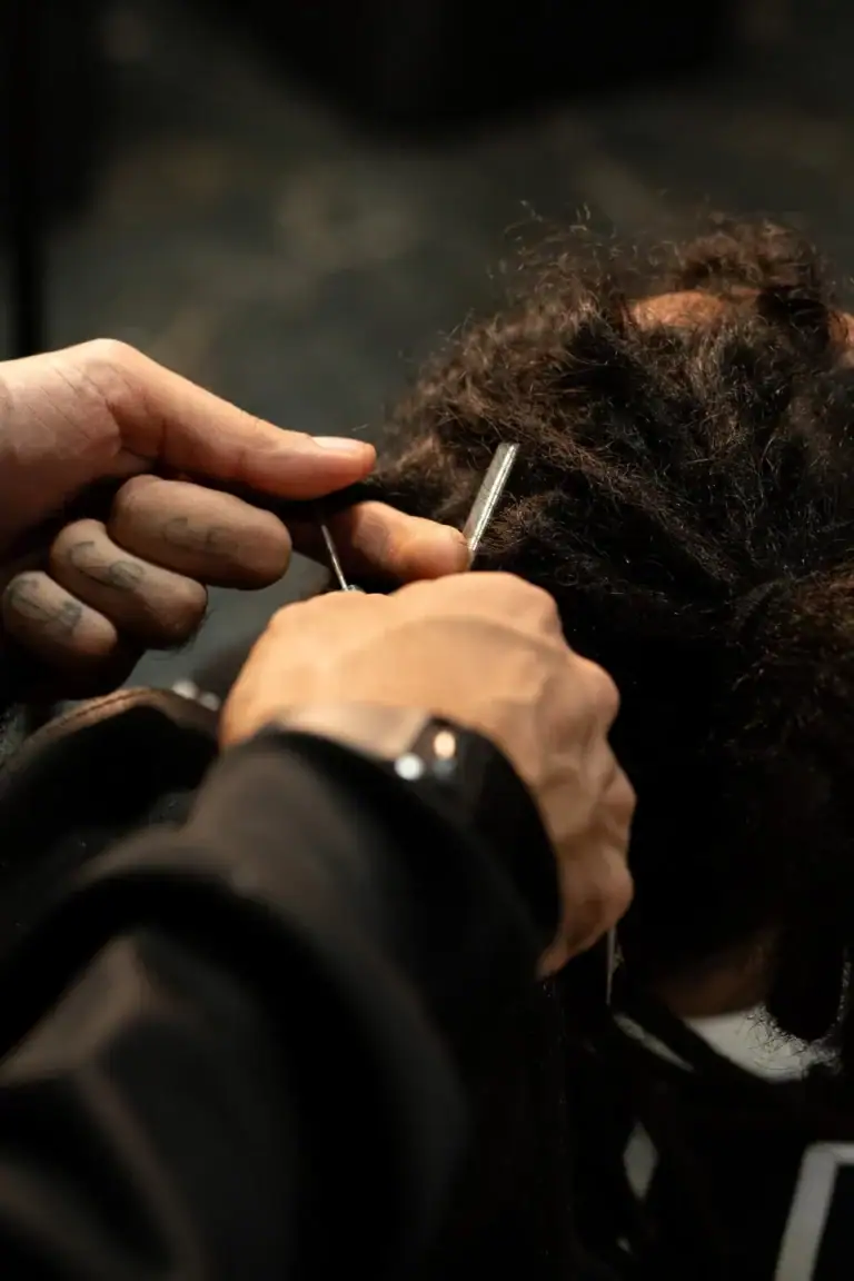 Cabeleireiro fazendo penteado em cliente com cabelo cacheado escuro.