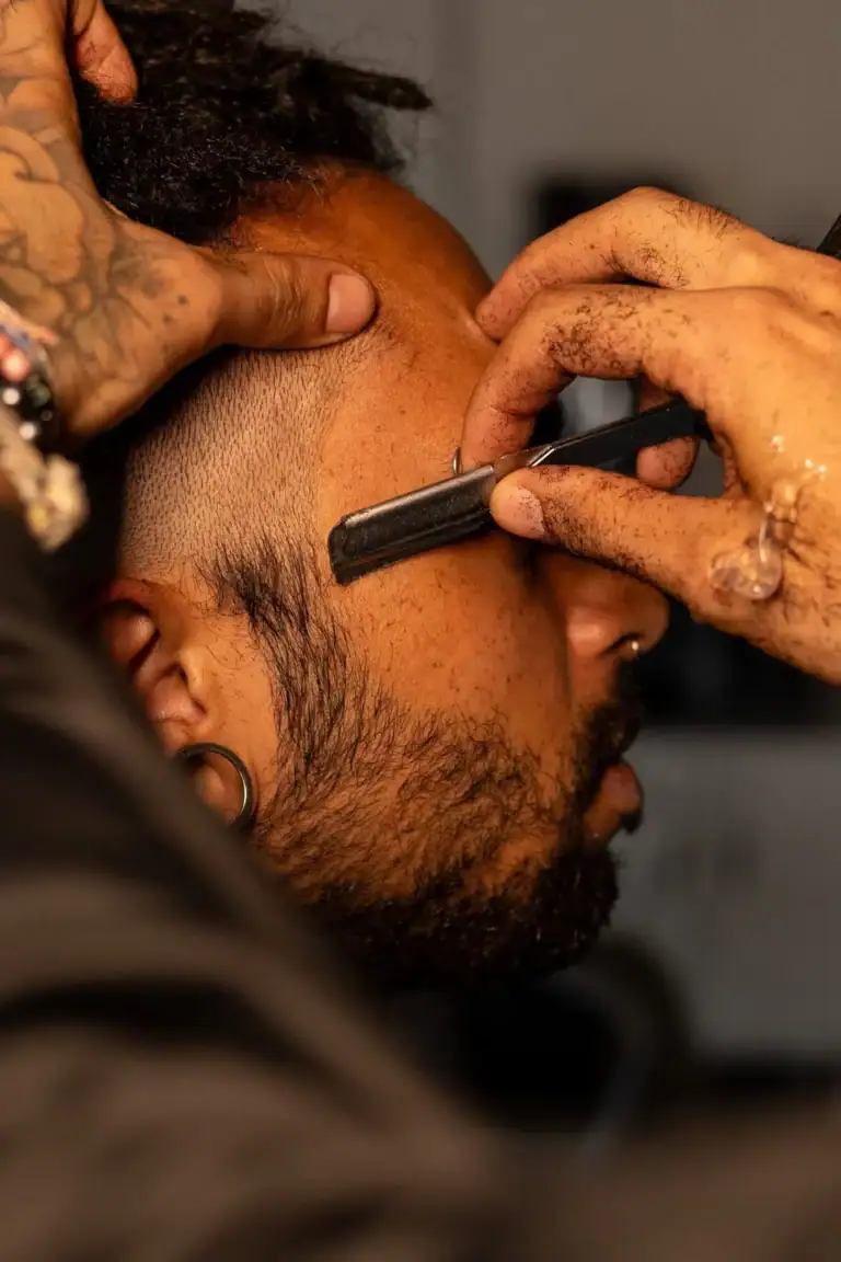Tatuador fazendo uma tatuagem na cabeça de um cliente.