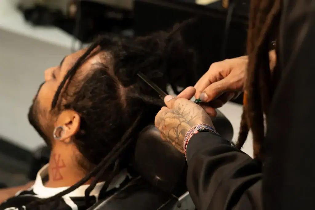 Barbeiro cortando cabelo de cliente com dreadlocks em barbearia moderna.