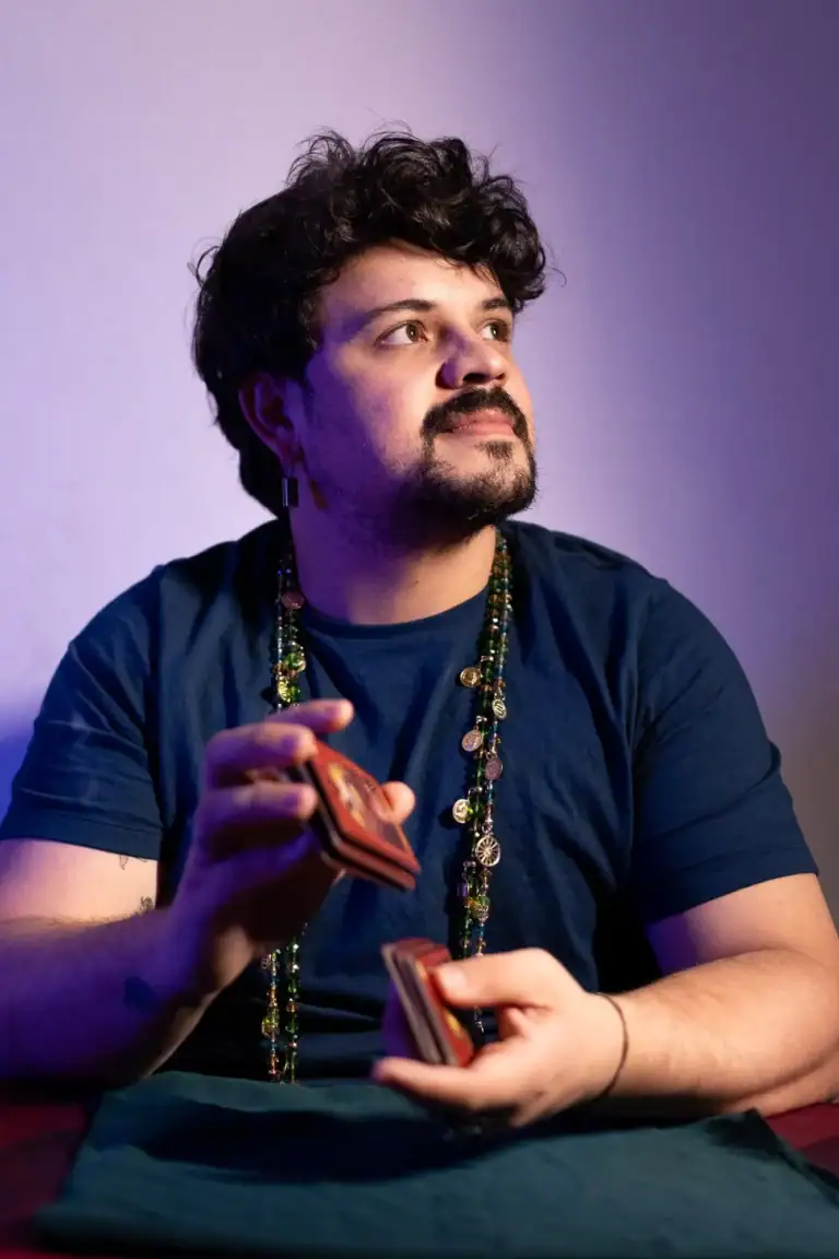 Fotógrafo Guilherme Marques com baralho, expressão pensativa, fundo colorido.