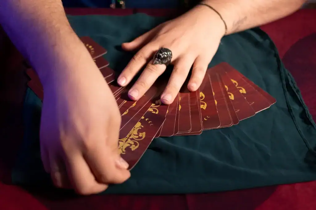 Mãos segurando cartas de tarô em uma mesa vermelha, foco na mão com anel.