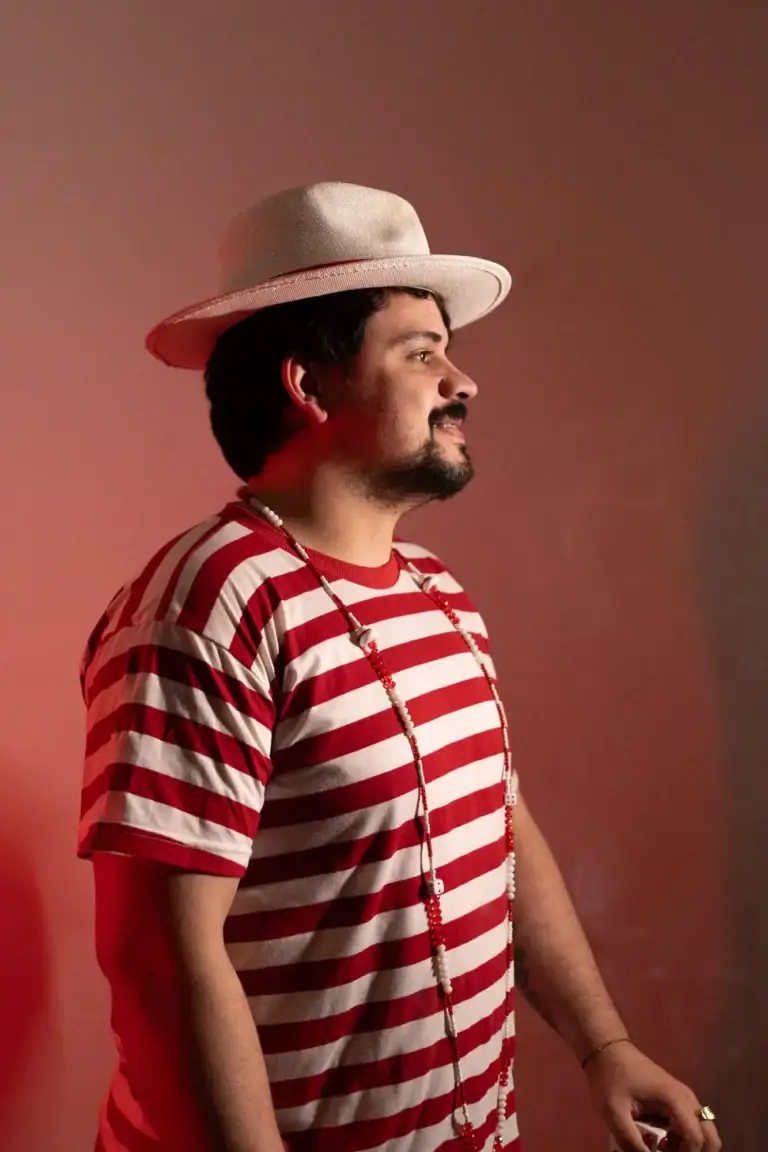 Homem com chapéu branco, camiseta listrada vermelha e branca, olhando para a direita.