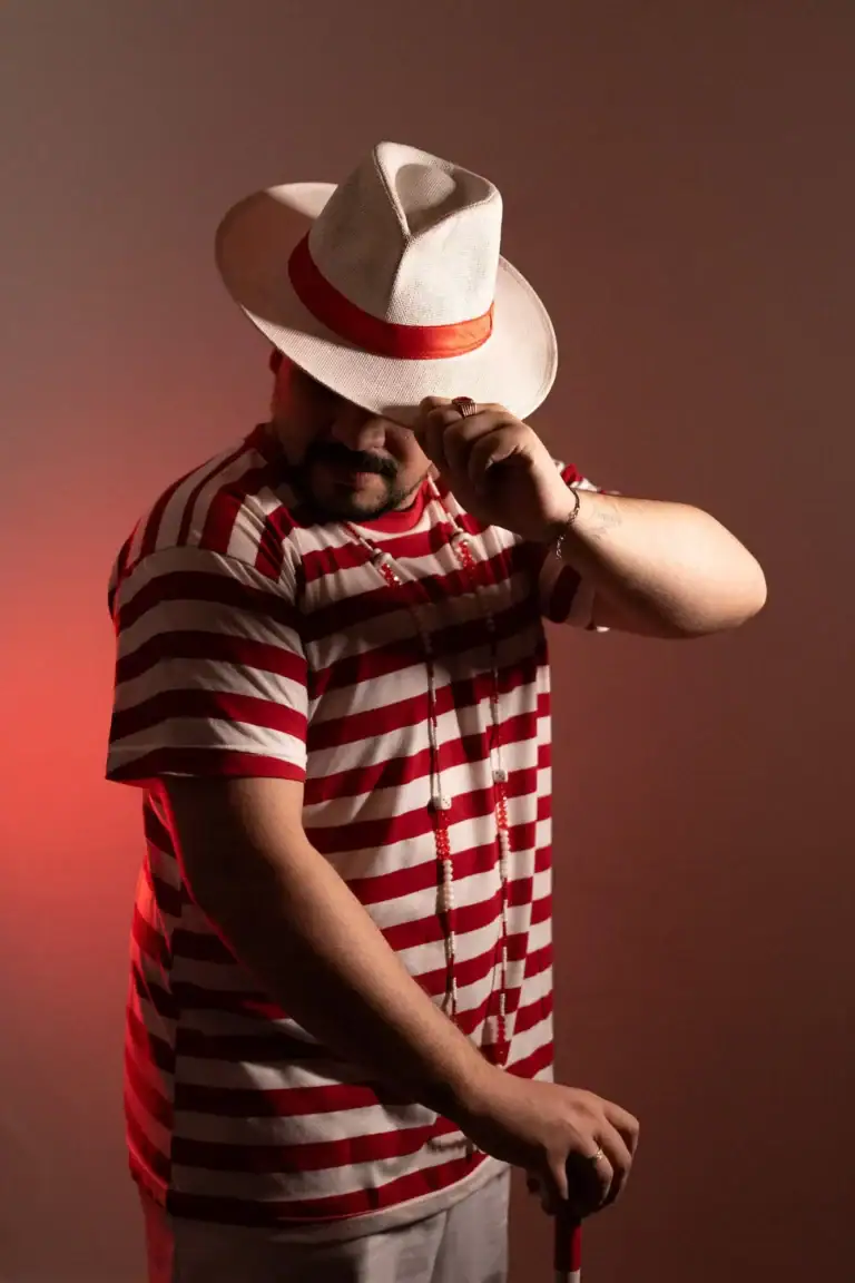 Homem com chapéu branco e camisa listrada vermelha e branca.