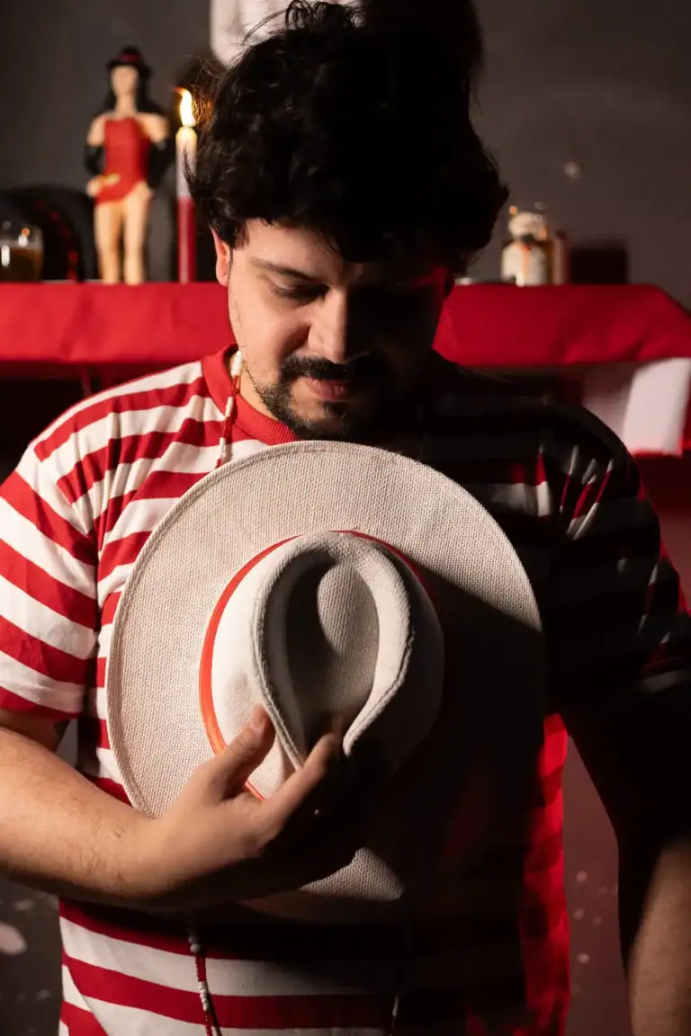Homem segurando chapéu com fundo de palco e figurino de show.