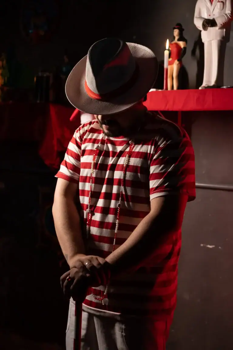 Homem com chapéu, camiseta listrada e bengala em ambiente de teatro ou show.