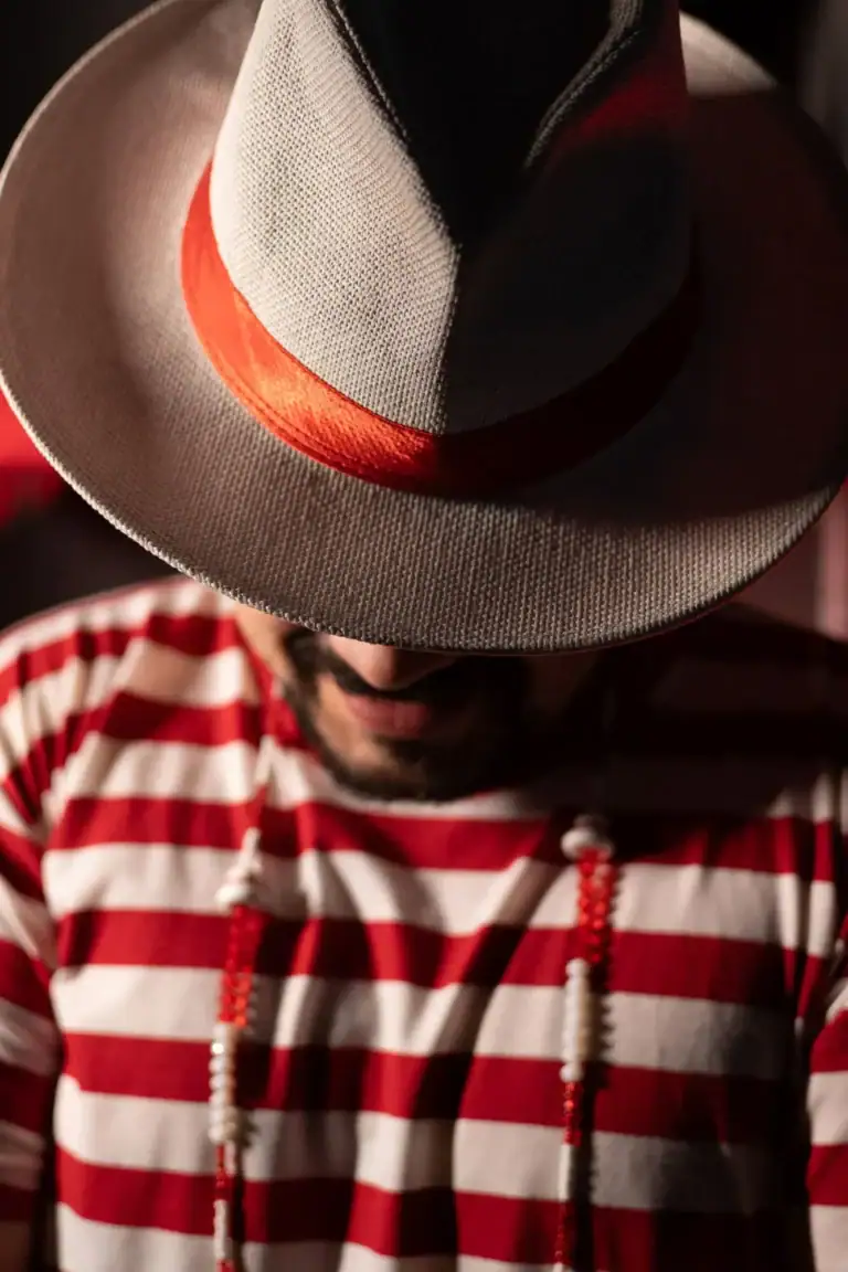 Homem com chapéu de coco e camisa listrada vermelha e branca.