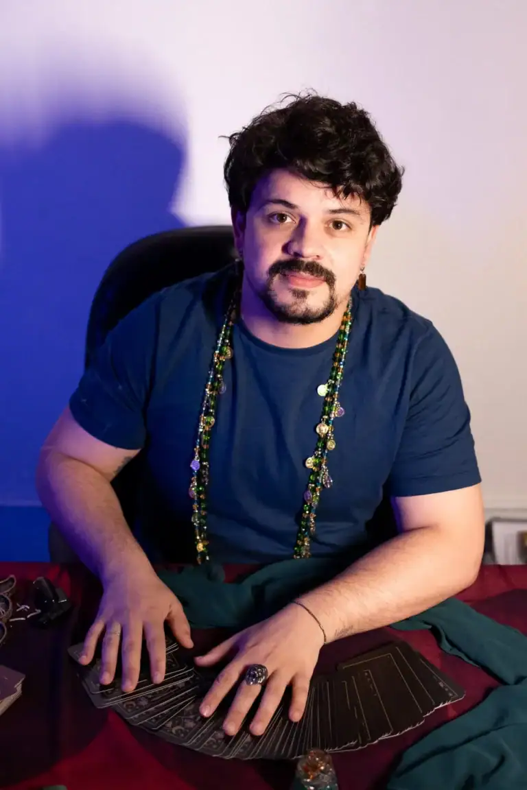 Fotógrafo Guilherme Marques com roupas casuais e acessórios, sentado em ambiente de estúdio.