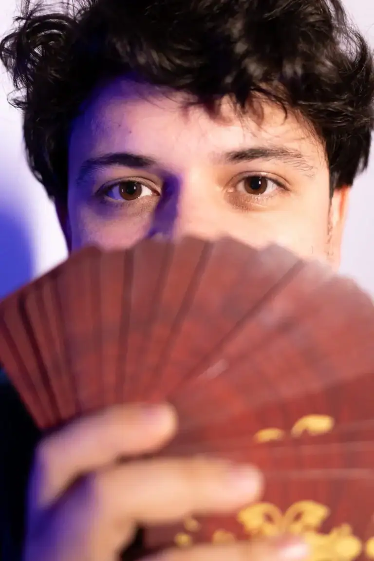 Jovem segurando baralho de cartas com foco no rosto e olhos expressivos.